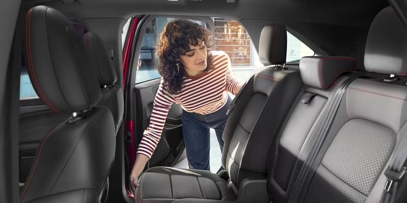 woman with curly hair and a red and white stripped shirt adjusting the back seat of a 2024 ford escape plug-in hybrid