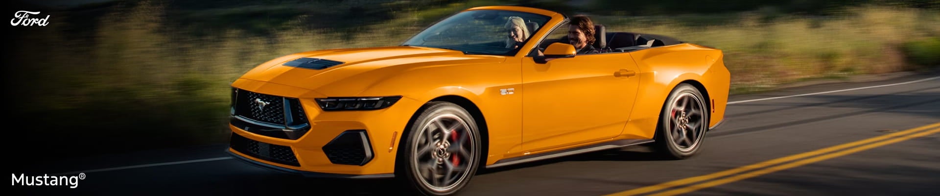 Orange Ford Mustang convertible driving on a road with the top down.